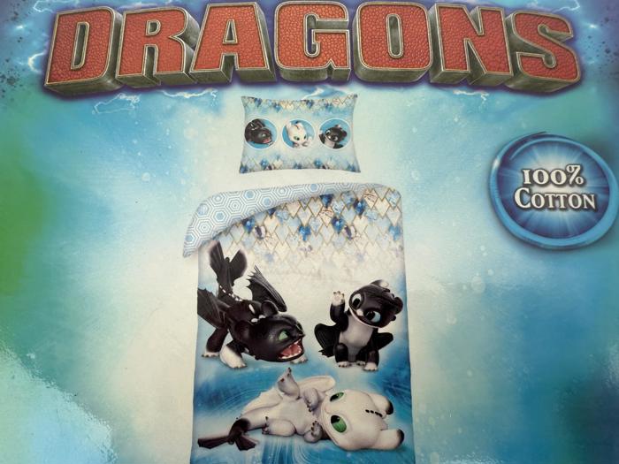 Et blåt Dragons-sengesæt med legende tegneseriedrager, tekst i 100 % bomuld til højre og lyneffekter i baggrunden.