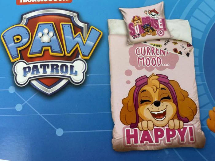 Et sengetøjssæt med PAW Patrol-tema med Skye, hvor der står CURRENT MOOD: HAPPY! på tæppet. Sengen er lyserød og ved siden af PAW Patrol-logoet på en blå baggrund.