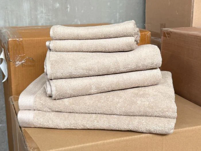 En pænt foldet stak beige håndklæder ligger oven på papkasser, med en grå væg i baggrunden.