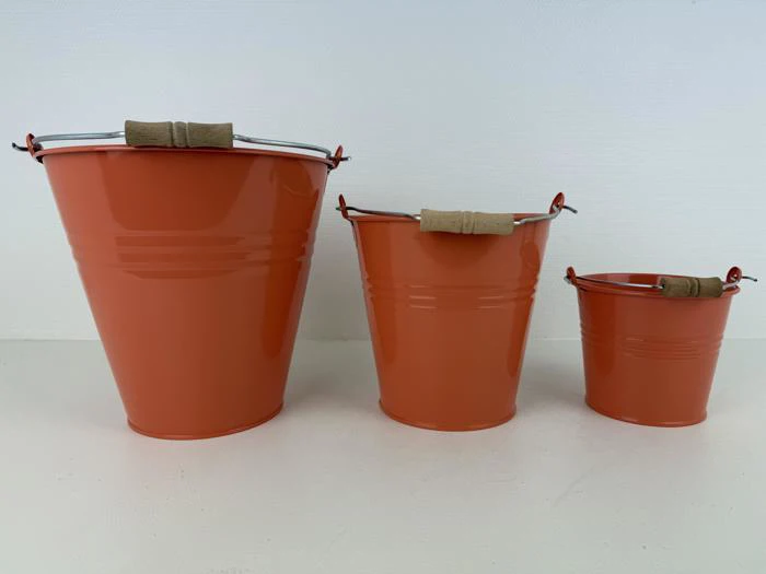 Tre orange metalspande i forskellige størrelser med træhåndtag er anbragt i en række på en hvid overflade mod en hvid baggrund.