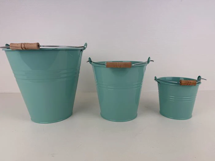 Tre turkise metalspande med træhåndtag er arrangeret i en række fra den største til den mindste på en lys overflade mod en ensfarvet baggrund.