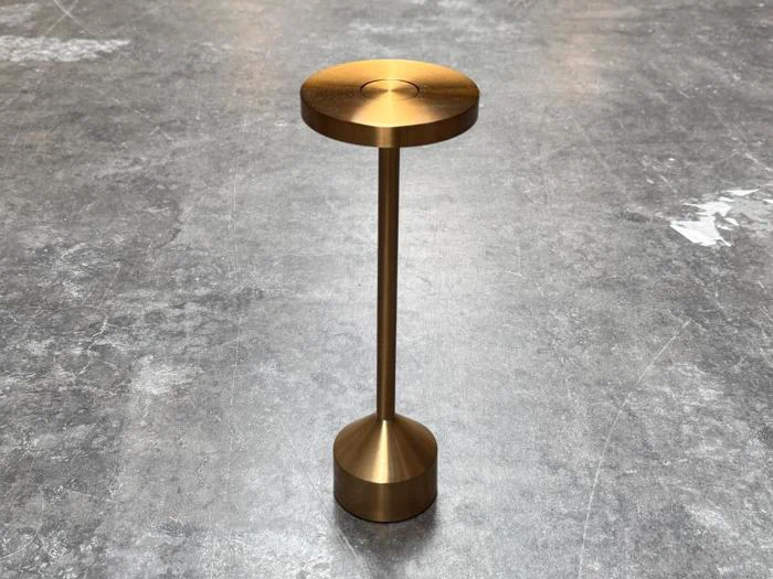 Et lille, rundt sidebord i metallisk guld står på et gråt betongulv.