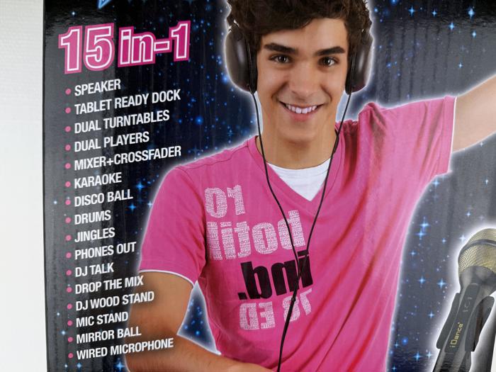 En smilende ung person iført hovedtelefoner og en lyserød skjorte står ved siden af en liste, der beskriver funktionerne i en 15 i 1 lydenhed, såsom højttaler, to pladespillere og karaoke.