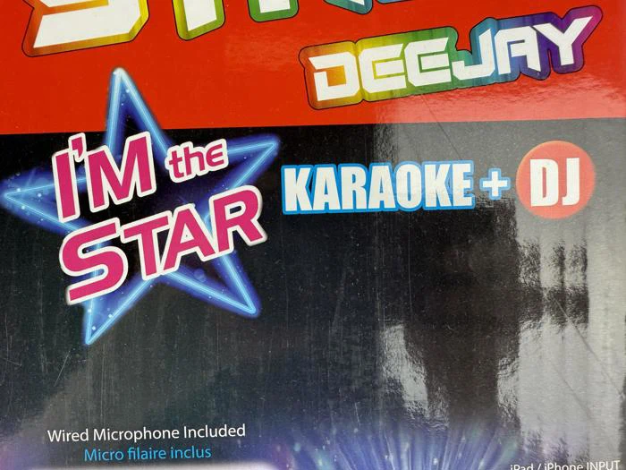 Farverig boks med teksten IM the STAR, KARAOKE + DJ og DEEJAY på en skinnende baggrund. Nederst står der, at der medfølger en mikrofon med ledning.