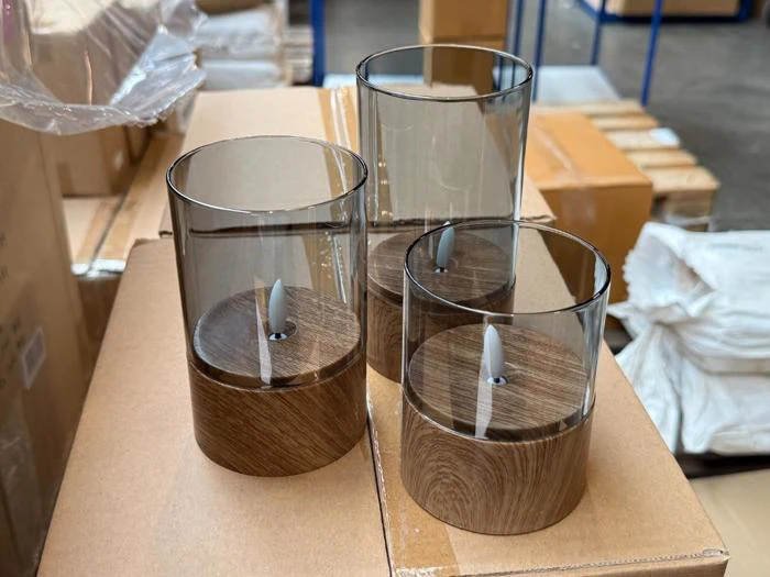 Tre cylindriske lysestager af glas med fod i trælook og LED-flammer i midten.