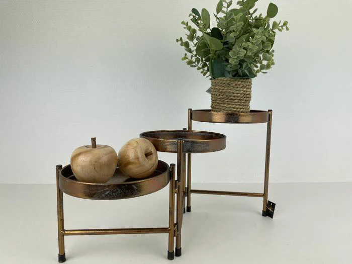 To-etagers bronzefarvet metalstativ med trææbler på den nederste bakke og en potteplante med grønne blade på den øverste bakke, mod en almindelig hvid baggrund.