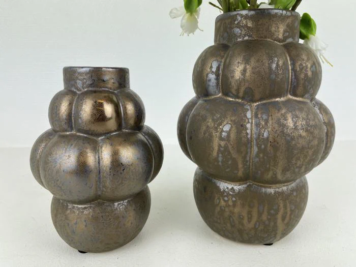 To metalliske, pæreformede keramikvaser med en struktureret, meleret overflade står på en hvid flade; den højeste vase indeholder et par hvide blomster.