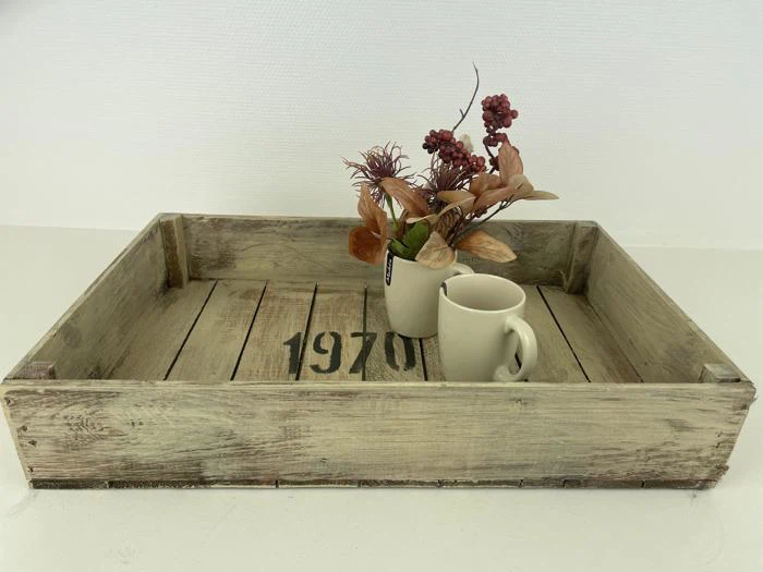 En rustik træbakke med mærket 1970 rummer et hvidt krus og en hvid vase med kunstige røde bær og brune blade.