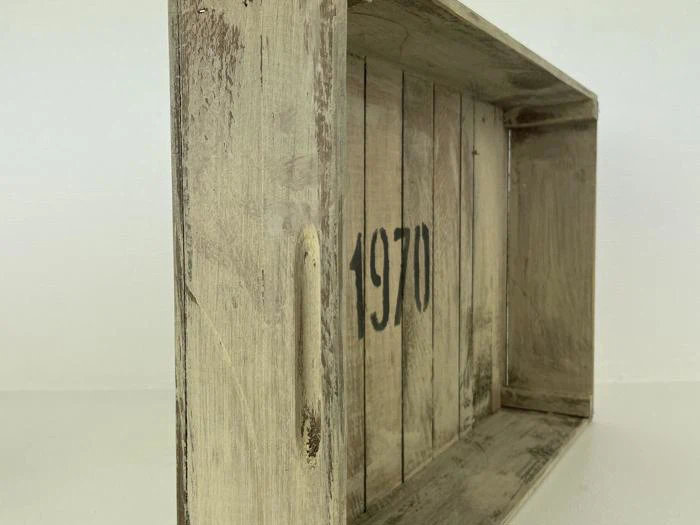 En rustik trææske med 1970 malet i sort på indersiden af bagpanelet, set fra en skrå side.