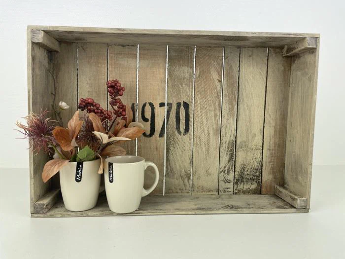 En rustik trækasse med 1970-maling på indersiden, der holder to flødekrus - det ene med kunstige efterårsblade og bær, det andet tomt.