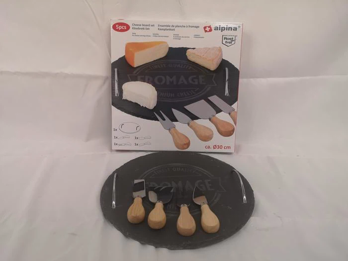 Et ostebræt med fire osteknive på et rundt sort skiferbræt, vist foran æsken med ostebilleder og produktoplysninger.