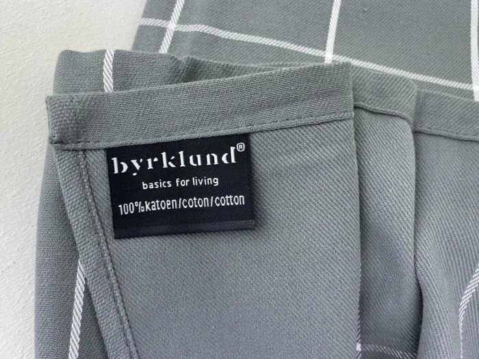 En grå stofvare med hvide striber har en etiket med teksten byrklund basics for living 100% katoen/bomuld/coton.
