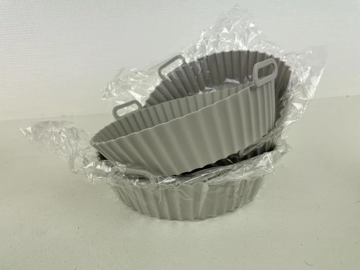 Tre grå, riflede silikoneforme stablet sammen, delvist pakket ind i klar plast, placeret på en lys overflade med en ensfarvet baggrund.