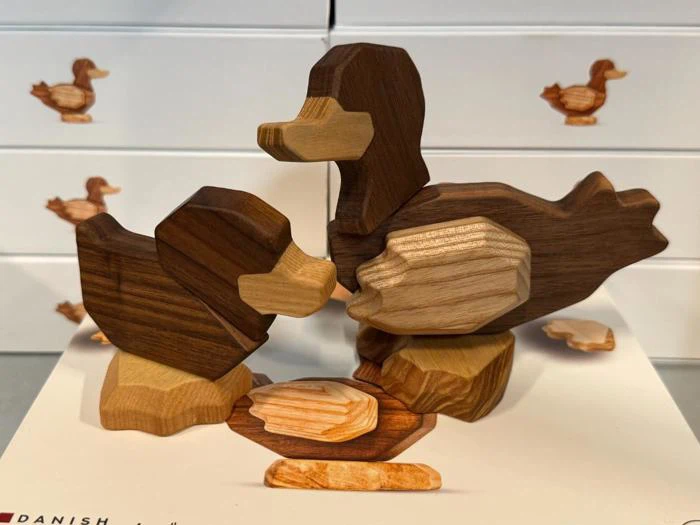 Træfigurer af en and og en ælling står ved siden af en rede med et æg, mens der i baggrunden ses kasser med andemotiver.