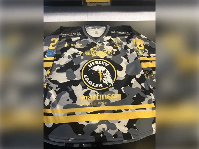 En Herlev Eagles-ishockeytrøje med et sort, gråt og gult camouflagemønster, holdlogoer, sponsornavne og nummeret 28 på begge ærmer og skuldre.