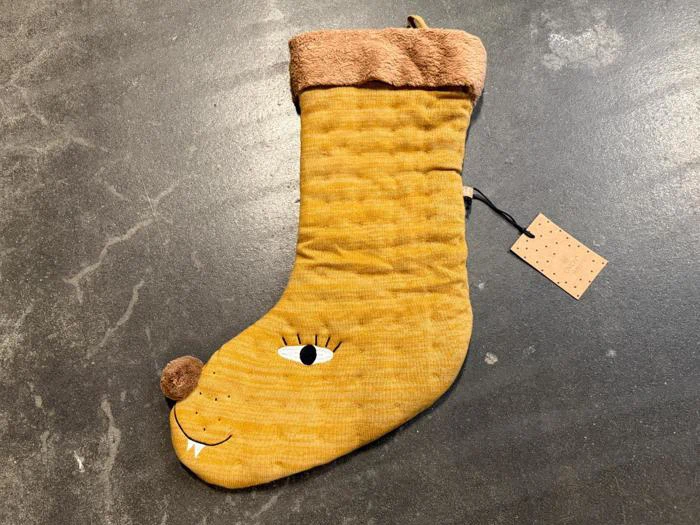 En gul julesok med et ansigt, et øje, øjenvipper, en brun næse og hugtænder, der ligger på en mørk overflade med en mærkat fastgjort.