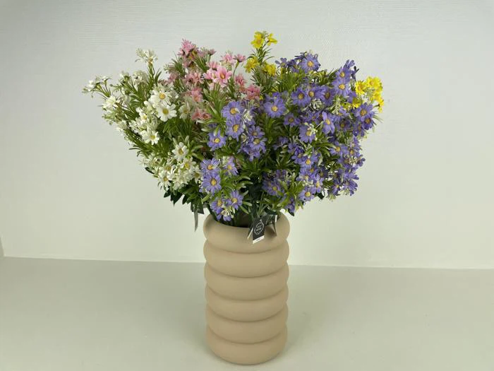 En beige, riflet vase med en buket hvide, pink, gule og lilla vilde blomster på en almindelig hvid baggrund.