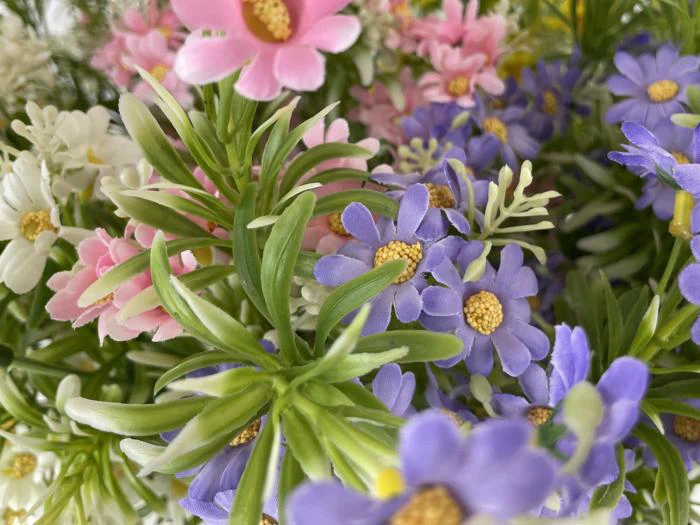 Et nærbillede af kunstige blomster i lilla, rosa og hvide nuancer omgivet af grønne blade og løv.