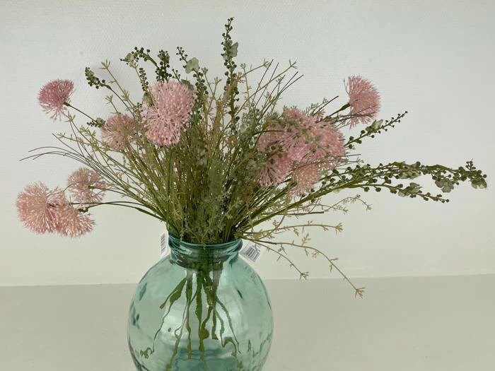 En buket lyserøde, runde blomster med grønne stilke i en lyseblå glasvase på en almindelig hvid baggrund.