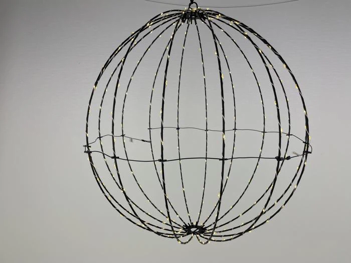 En kugleformet wireframe-struktur dekoreret med små lyskæder, der hænger op ad en almindelig hvid væg.