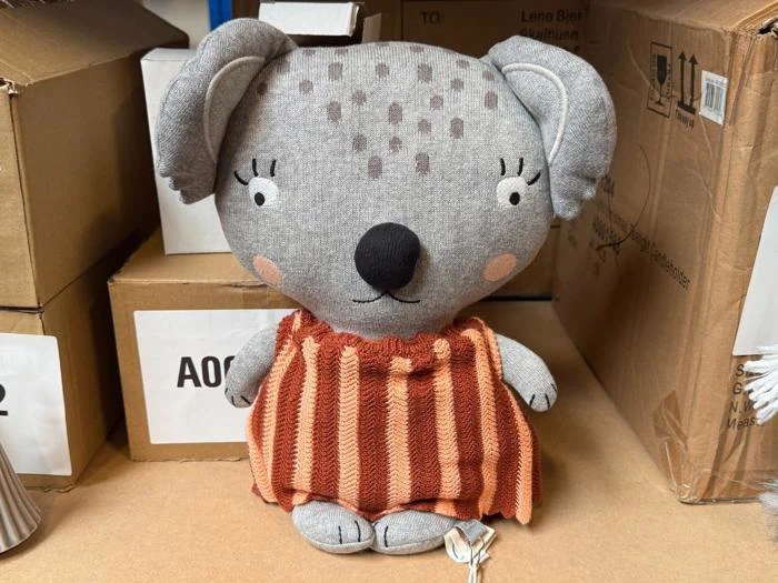 Et koala-plysdyr af gråt stof, der har en rustfarvet stribet kjole på.