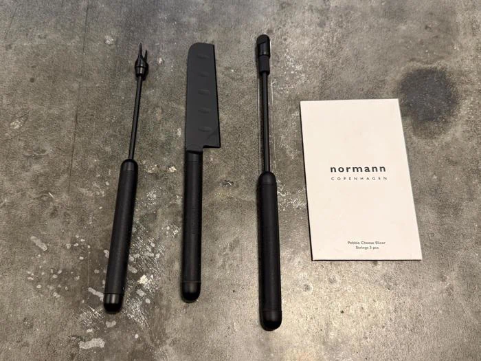 Tre sorte osteknive ved siden af et produktkort fra Normann Copenhagen.