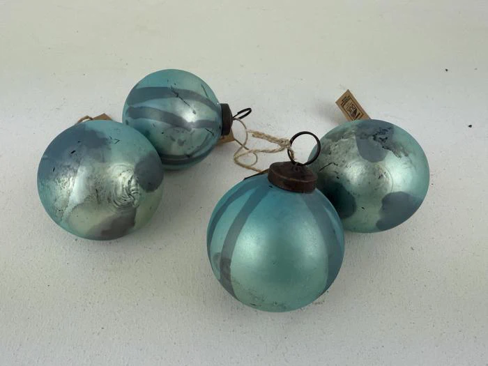 Fire blå glasjulekugler med sølvstriber og brune metaltoppe, der hviler på en hvid overflade.