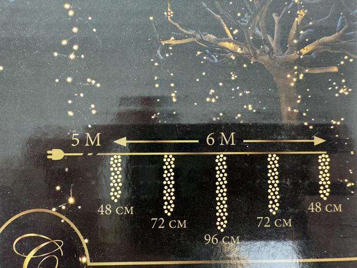 Diagram, der viser en lyskæde: 5 meter uden lys, derefter 6 meter lys i fire sektioner med mellemrum på 48 cm, 72 cm, 96 cm og 72 cm mellem lysene; et træ med lys i baggrunden.