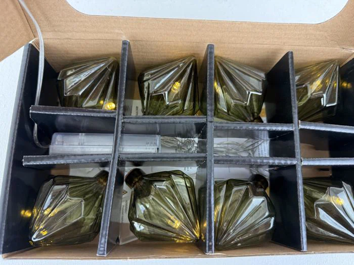 En æske med otte mørkegrønne, facetterede glasbægre, hver adskilt af papskiver.