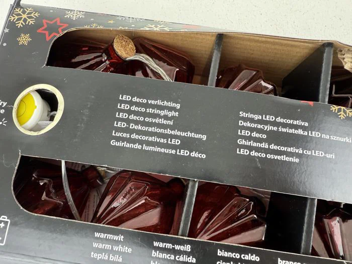 En æske med røde, stjerneformede, dekorative LED-lyskæder med mærkning på flere sprog på emballagen.