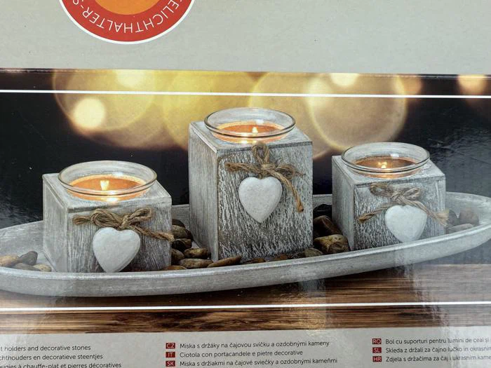 Tre rustikke lysestager med hjerteornamenter og lys indeni, udstillet på en bakke med dekorative sten og varme, slørede lys i baggrunden.