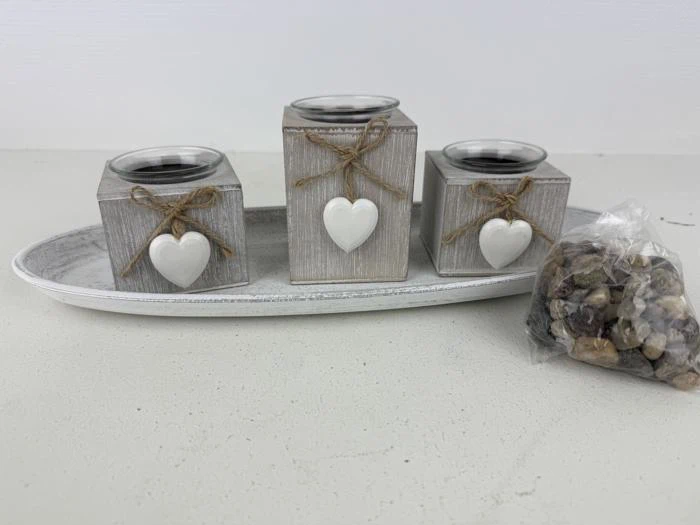 Tre rustikke trælysestager med hjerteornamenter og sejlgarnssløjfer, placeret på en bakke ved siden af en lille pose med dekorative sten.