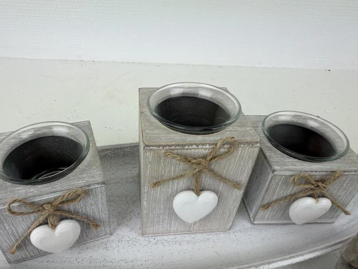 Tre trælysestager i forskellige højder, hver dekoreret med et hvidt hjerte og en sløjfe af sejlgarn, placeret på en hvid bakke mod en lys baggrund.