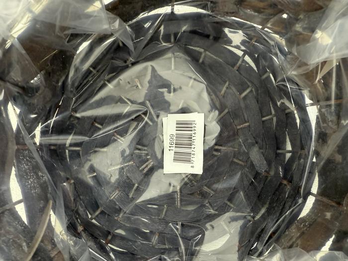 En flettet kurv med mørke striber, set ovenfra, pakket ind i klar plast med et stregkodeklistermærke i midten.