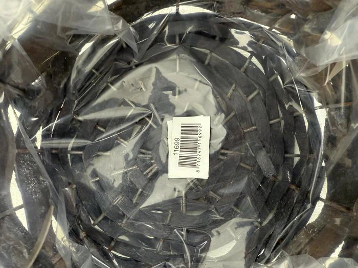En flettet kurv med mørke striber, set ovenfra, pakket ind i klar plast med et stregkodeklistermærke i midten.