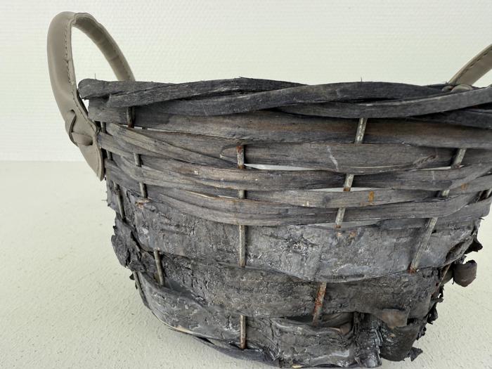 Nærbillede af en rustik, forvitret flettet kurv med grålige, slidte strimler og to hanke på en almindelig lys baggrund.