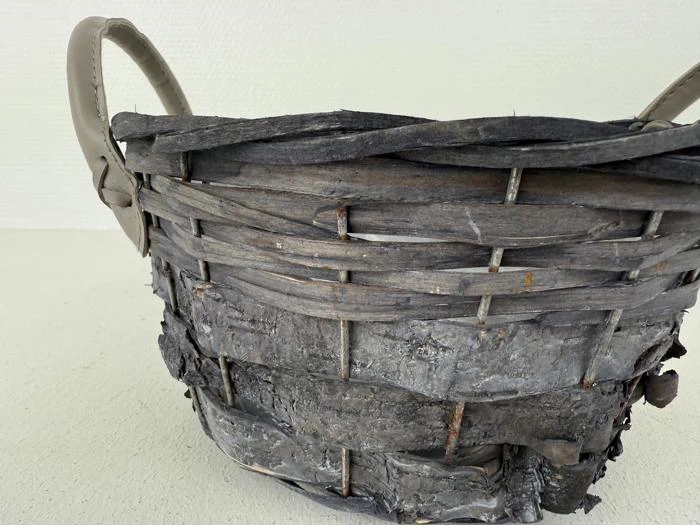 Nærbillede af en rustik, forvitret flettet kurv med grålige, slidte strimler og to hanke på en almindelig lys baggrund.