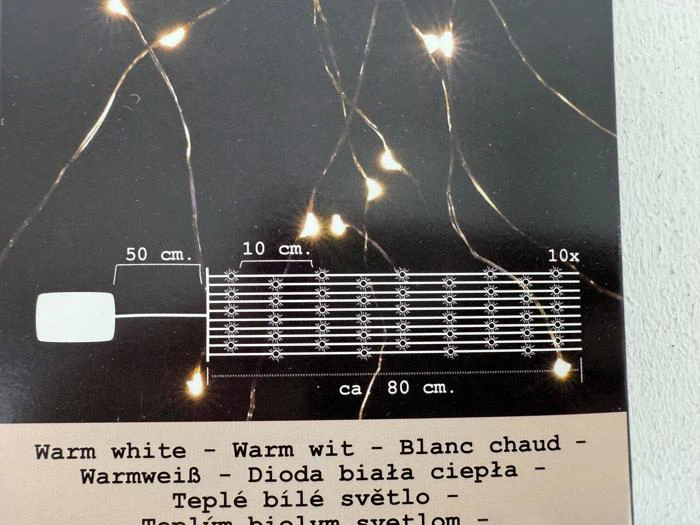 Et diagram over en lyskæde med 10 pærer med 10 cm mellemrum over en længde på 80 cm plus en 50 cm lang ledning; beskrevet på flere sprog nedenfor.