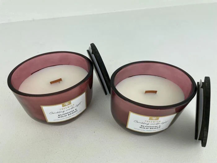 To lilla glaslys med trævæger og sorte låg, mærket Trewick Blossom & Wild Berry, står på en hvid flade.