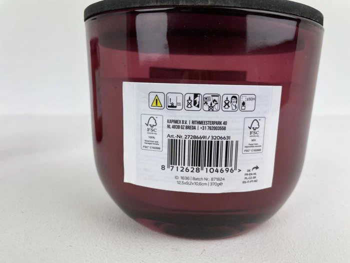 Nærbillede af bunden af en rød plastbeholder med sort låg, der viser en hvid etiket med stregkoder, produktinformation, advarselssymboler og genbrugsikoner.