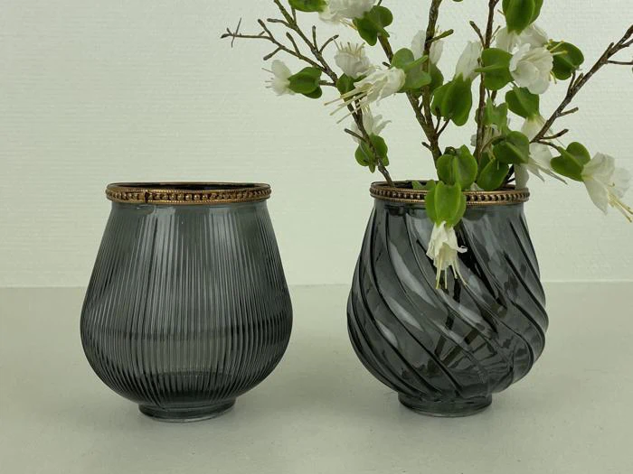 To grå glasvaser med guldkant; den ene vase er riflet og tom, den anden har et spiralmønster og indeholder hvide blomster med grønne blade.