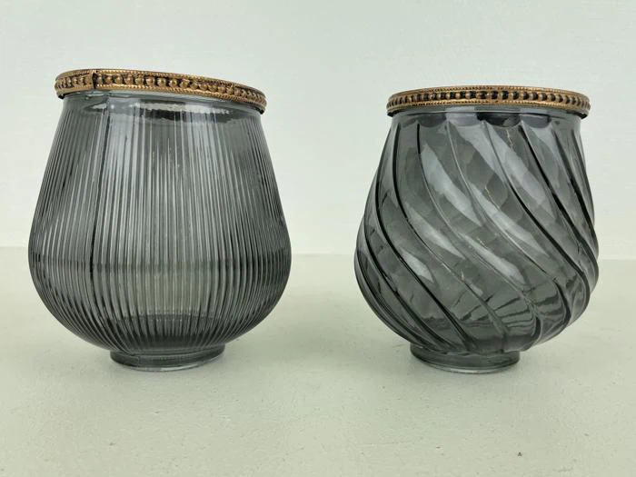 To grå glaskopper med guldkant; den venstre kop har lodrette riller, og den højre kop har et spiralmønster. Begge står på en lys overflade.