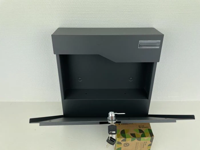 En sort metalpostkasse med et åbent frontpanel, en lås og to nøgler står på en hvid flade op ad en hvid væg. En papkasse er placeret under det åbne panel.