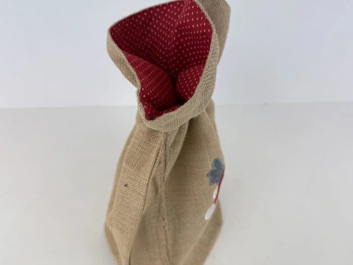 En jutepose med rødt, prikket stoffor indeni, der står oprejst på en hvid overflade.