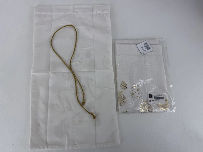 To hvide stofposer, den ene med guldsnor og den anden pakket i plastik med synlige gulddekorationer på indersiden af emballagen.