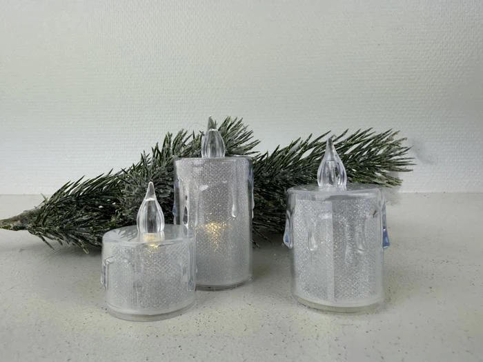 Tre batteridrevne LED-lys med matteret finish er placeret foran en fyrretræsgren på en hvid flade mod en lys struktureret væg.