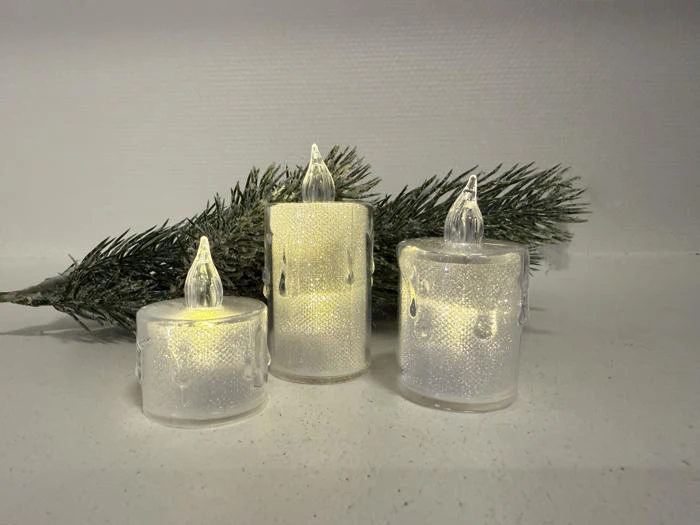 Tre batteridrevne LED-lys med matteret overflade lyser blødt foran en lille fyrretræsgren på en hvid flade.