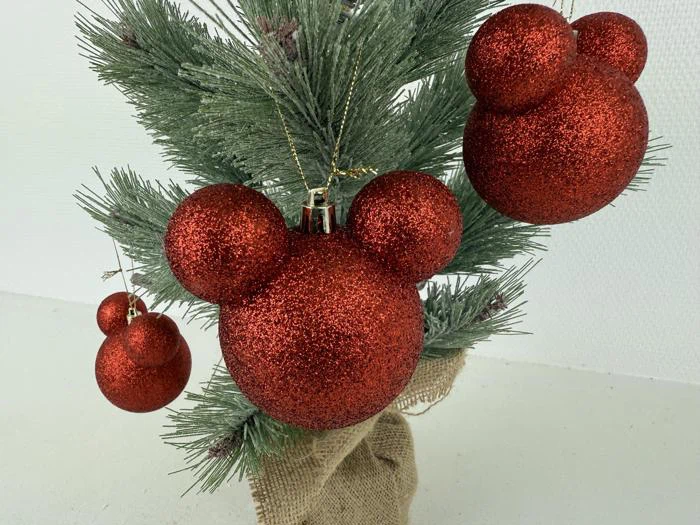 Et lille juletræ pyntet med røde glitrende ornamenter formet som Mickey Mouse-hoveder.
