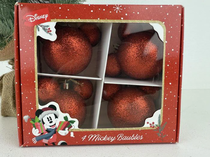 En rød æske med Disney-branding indeholder fire røde, glitrende Mickey Mouse-formede julekugler, mærket 4 Mickey Baubles. Æsken er dekoreret med en tegning af Mickey, der holder gaver.
