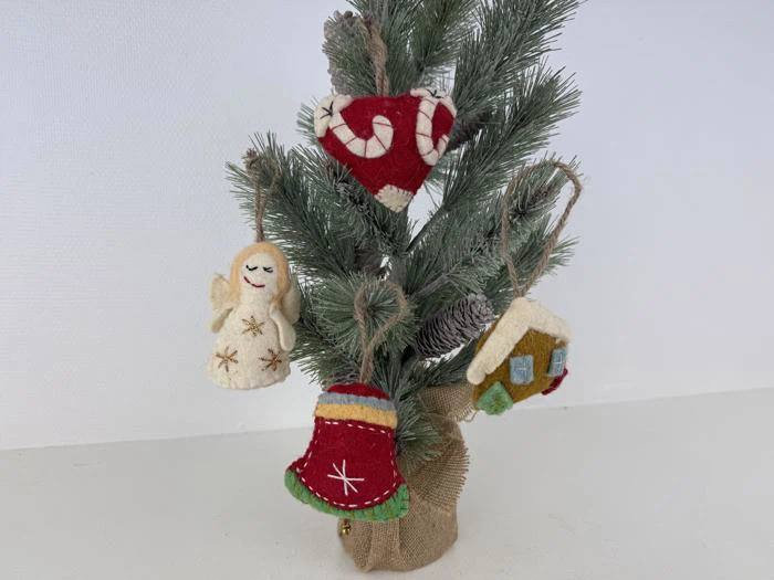 Et lille kunstigt juletræ med filtpynt: en engel, et rødt hjerte, en rød klokke og et hus, alt sammen dekoreret med festlige mønstre.